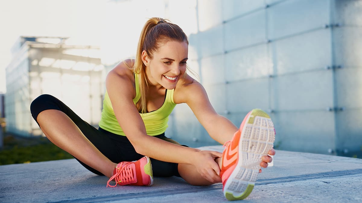 Happy young woman stretching before running outdoors