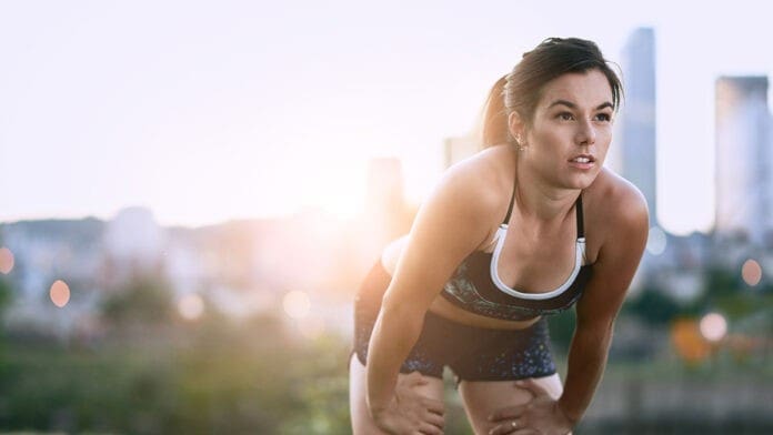 Portrait of active millenial woman jogging at dusk with an urban cityscape and sunset in the background