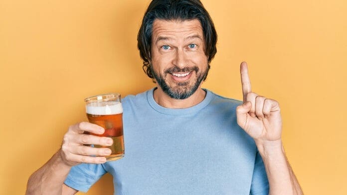 Middle age caucasian man drinking a pint of beer smiling with an idea or question pointing finger with happy face, number one